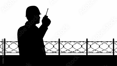 Silhouette of a security guard in a hard hat communicating with a portable radio transceiver while standing near a barbed wire fence representing surveillance and protection