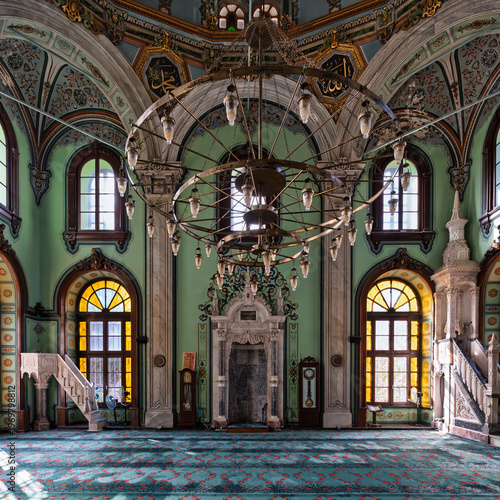 Salepcioglu Mosque interior, Izmir, Turkey. Ornate chandelier, mihrab, minbar, arched windows with stained glass, intricate Islamic calligraphy and floral patterns on walls and ceiling