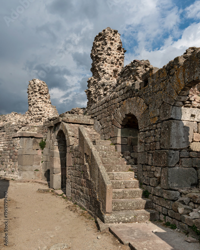 Ancient stone ruins with a staircase and arched doorways at the Acropolis of Pergamon, Bergama, Turkey under a cloudy sky