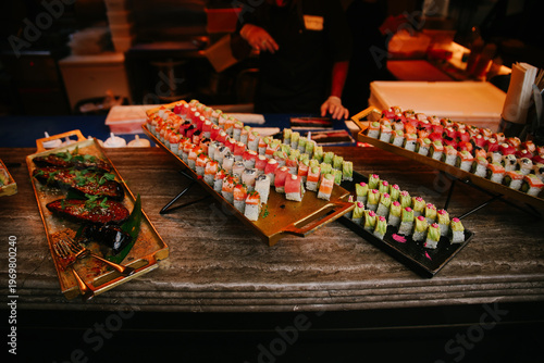 Horizontal Wide Shot of a Luxury Sushi Buffet with Assorted Rolls, Miso Eggplant, and Professional Chefs in a High-End Event Setting
