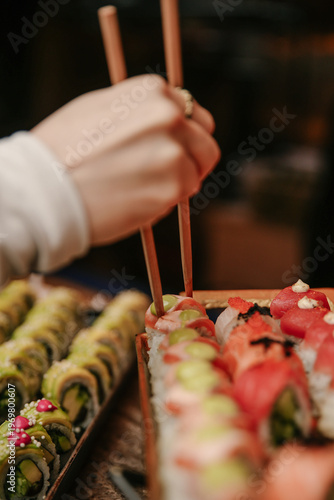 Vertical Close-up of a Guest Using Wooden Chopsticks to Pick Up Fresh Nigiri and Maki Sushi from a Gourmet Catering Display