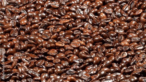 Horizontal rotating macro background of roasted coffee beans under hard lighting. Dramatic glossy texture for energetic cinematic cafe projects.