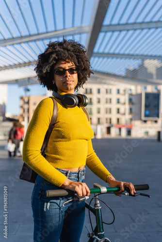 Young woman with headphones pushing bicycle in urban setting