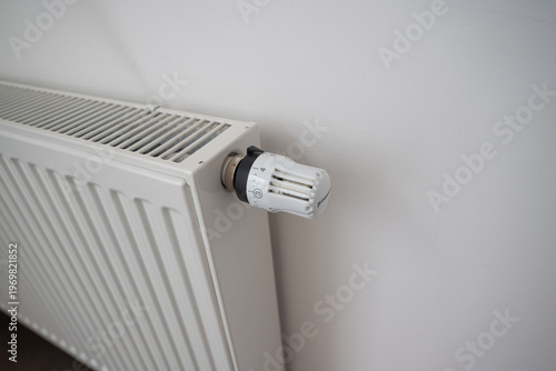 Heating radiator. A modern white radiator.  Heating concept. Adjusting temperature on heating radiator thermostat, Turning heat radiator knob to control heat in home.