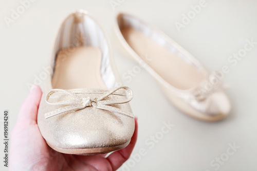 A young woman holds a single golden ballet flat, with the second one visible in the background. The photo is a metaphor for youthful dreams and the desire to set out into the wide world.