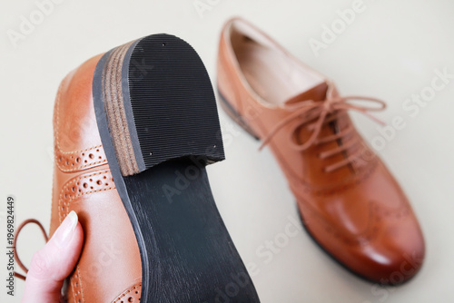 A woman holds a single Oxford shoe in her hand, with the other shoe of the pair visible in the background. The photo metaphorically represents a person appreciating luxury