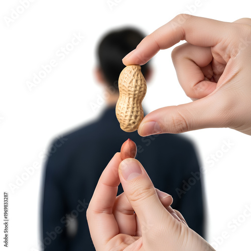 Hands holding peanut and peanut shell with blurred person in background.
