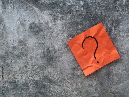 Question mark symbol on orange crumpled paper note over concrete wall background. Symbolizing confusion, curiosity, problem-solving, or seeking answers in a professional or creative context