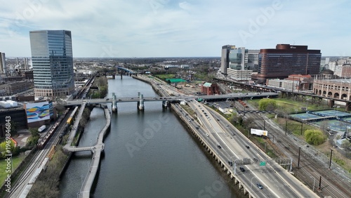 Aerial view of the Schuylkill River reflecting the sky, flowing under bridges and past modern buildings, with a highway bustling with traffic, Philadelphia, Pennsylvania, United States.