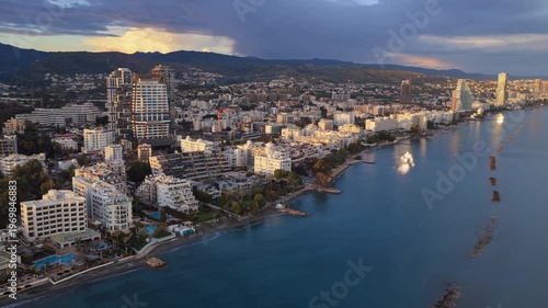 Aerial drone view of modern high rise buildings in Limassol illuminated by warm golden hour sunlight with mountains in the background