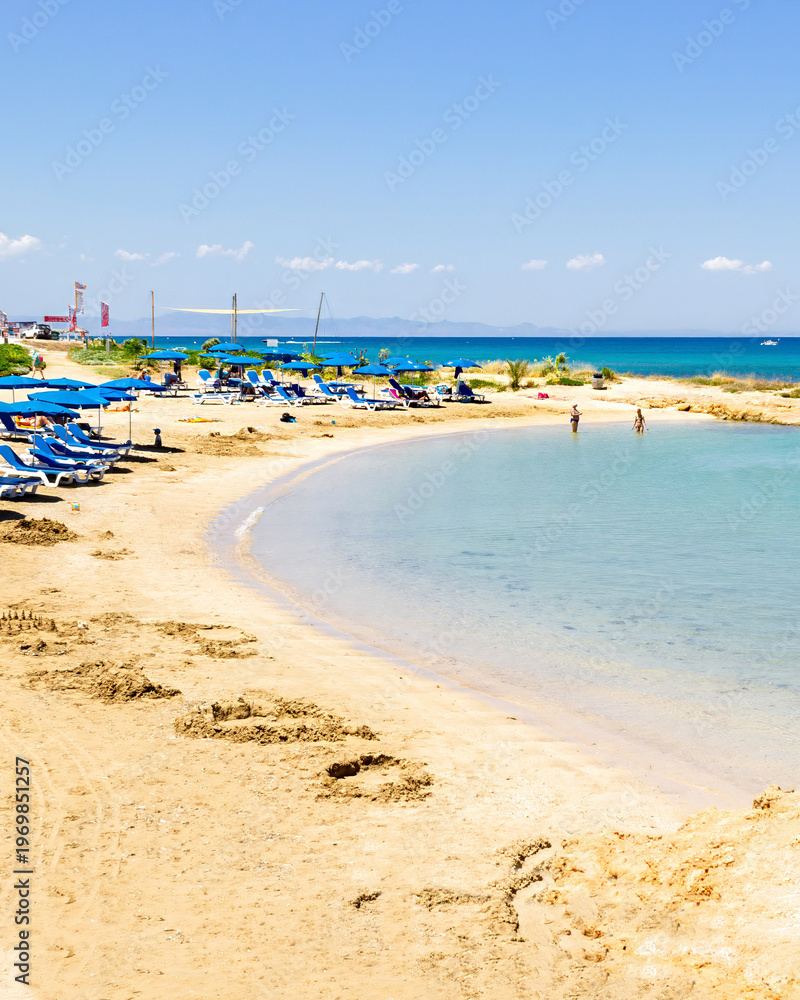 Obraz premium Crystal clear turquoise sea in a small rocky bay near Fig Tree Beach in Protaras, Cyprus on a sunny summer day. Calm shallow water, sandy shoreline and copy space create a perfect travel and vacation 