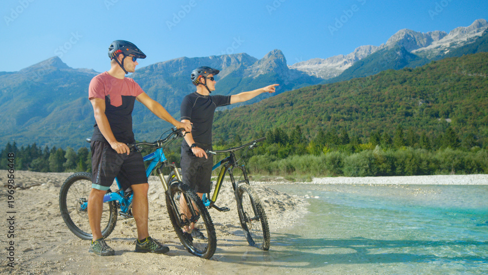 Fototapeta premium Guys riding bicycles talking and planning their route while standing by river.
