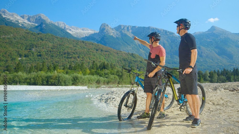 Fototapeta premium Cross country bikers stand by a stream and look around the picturesque nature.