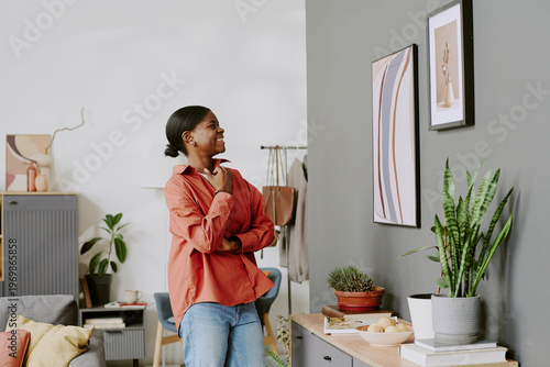 Obraz na plátně African American young adult woman examining framed wall art at home, comparing decor choices and planning interior styling