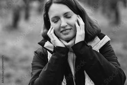 Pretty caucasian woman in her 40s with dark hair wearing warm clothes listening to music outdoors using earbuds and phone. Mature female enjoying her personal time, dancing and breathing fresh air.