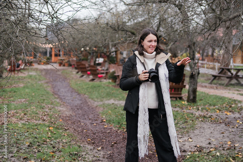 Caucasian woman photographer in her 40s wearing warm clothes taking photos of her friend in autumn park. Relaxed mature females spending time outdoors, enjoying leisure time, walking and posing.