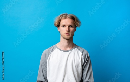Young blonde man with casual style standing against a solid blue background, portraying calm confidence and thoughtful expression for various media concepts