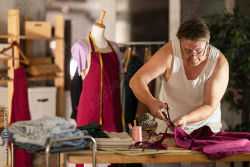 Canvastavla Middle-aged male dressmaker cutting textile in sewing workshop