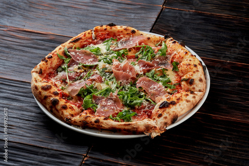 Canvas Print Top view of a Neapolitan pizza topped with prosciutto ham, fresh arugula, and grated parmesan cheese on a dark wooden background