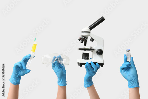 Female hands with modern microscope, ampule and syringe on grey background