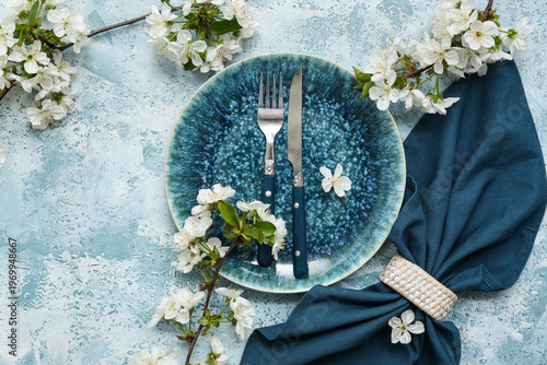 Beautiful table setting with blooming branches on blue background