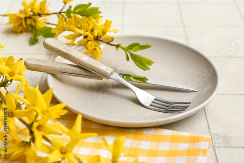 Beautiful table setting with yellow blooming branches on white tile background, closeup