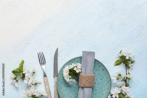 Beautiful table setting with blooming branches on light blue background