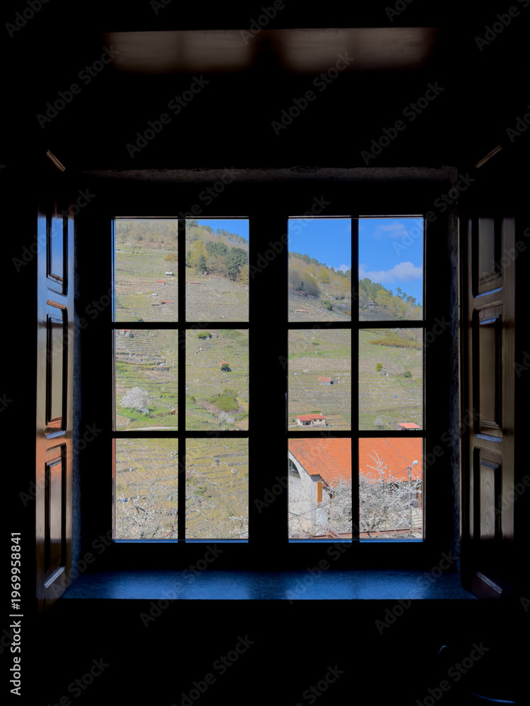 Fototapeta premium View from a dark room through a wooden-framed window onto a green hill