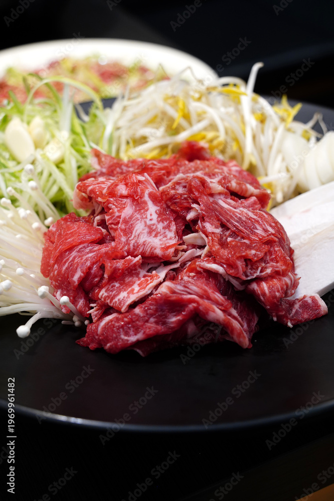 Fototapeta premium Fresh raw beef bulgogi with assorted vegetables including green onions, bean sprouts, and enoki mushrooms on a black plate, traditional Korean marinated beef preparation before cooking