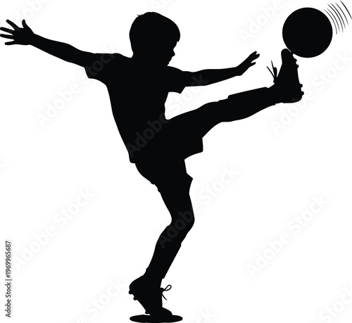Silhouette of a young boy kicking a soccer ball in midair during a game