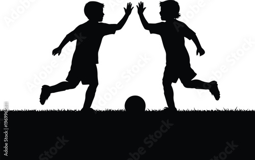 Two young boys silhouette playing soccer on a grassy field giving a high five
