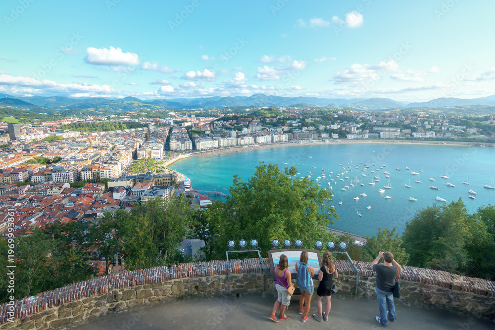 Naklejka premium Tourists enjoying panoramic view of La Concha bay from Monte Urgull in San Sebastian, popular viewpoint in Basque Country, Spain