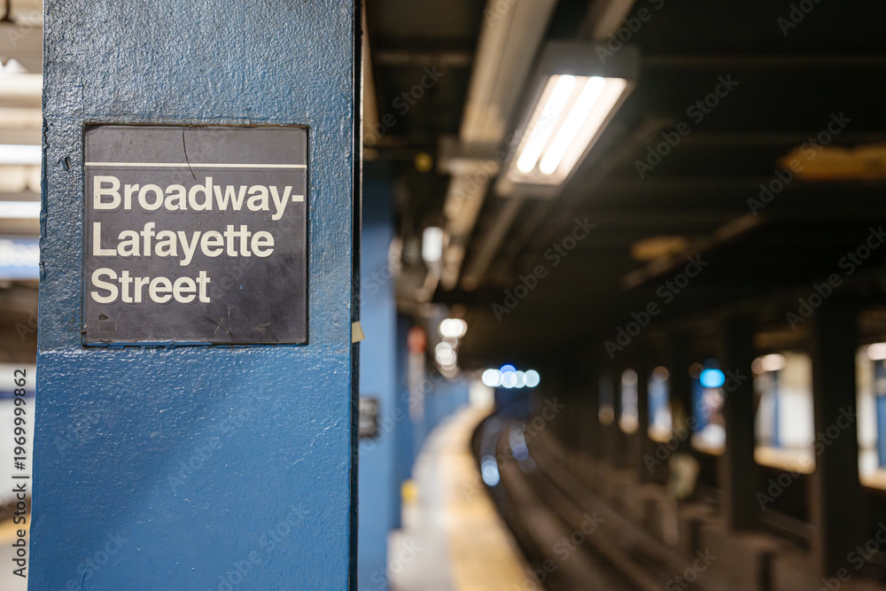 Fototapeta premium New York City, New York, USA - 08.03.2024: Close view of Broadway Lafayette Street subway station sign on blue steel column in Manhattan. Underground New York City metro platform with blurred railway