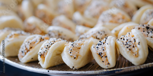 A close-up of a tray of bite-sized pastries filled with shredded filling and topped with sesame seeds, ideal for a buffet or party.