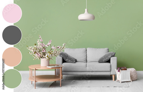 Sofa with coffee table, chandelier and vase of blooming branches near green wall in living room