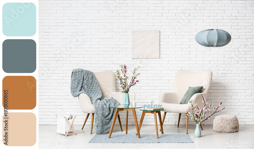 Armchairs with coffee tables, different decor and vases of blooming branches near white brick wall in living room