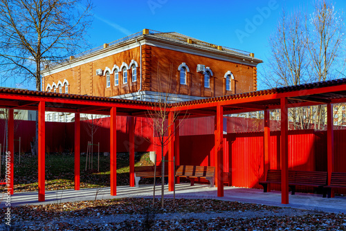 Modern urban environment design: vibrant red pergolas and seating areas in a city park. Concept of comfortable urban living and high-quality landscaping.