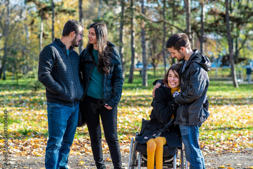 Young woman in a wheelchair with her boyfriend and friends in a park. Two couples