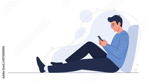Young man in glasses using smartphone, sitting relaxed on floor, blue sweater