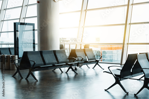Empty airport terminal with waiting seats and bright sun shining through large windows