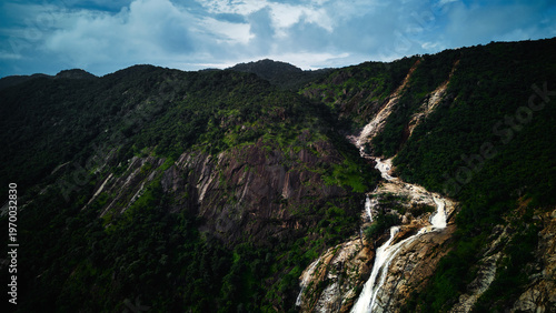 Aerial view of a cascade of water tumbling down a rocky slope amidst lush green vegetation, contrasting against the cloudy sky, Nasarawa, Nasarawa, Nigeria.