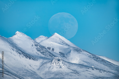 Full moon rising at dusk over snow covered peaks Iceland