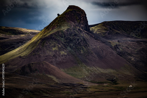 A towering volcanic mountain looms over a small house in Iceland