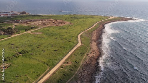 Aerial drone view of walking path along coastline with green landscape and sea waves in Paphos, Cyprus