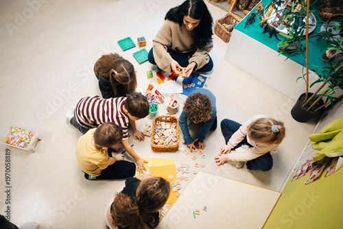 High angle view of female teacher sitting with elementary children doing fun activity in classroom at preschool