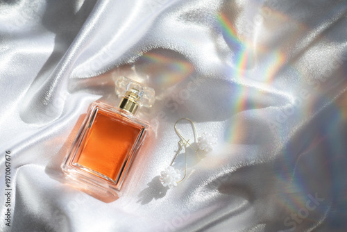 Luxury women’s perfume with elegant earrings on silk background, premium beauty and fashion concept