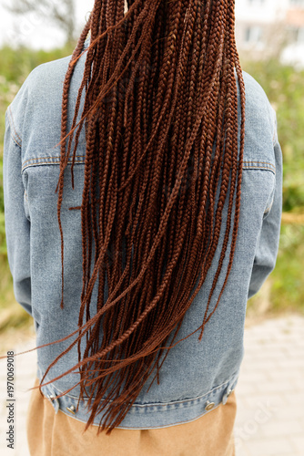 Rear view of a person with long reddish-brown box braids or dreadlocks wearing a blue denim jacket outdoors, close up for hairstyle, ethnic beauty, fashion, and hair care concept. vertical