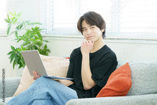 ソファに座ってノートパソコンを操作する若い日本人男性