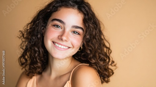 Happy young woman with natural curly hair smiling brightly at viewer on simple warm background