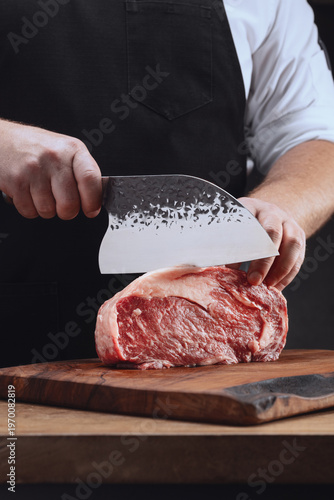 Male yands cutting raw beef meat. Male hands holding a large knife and cutting a piece of raw meat on a cutting wooden board. 